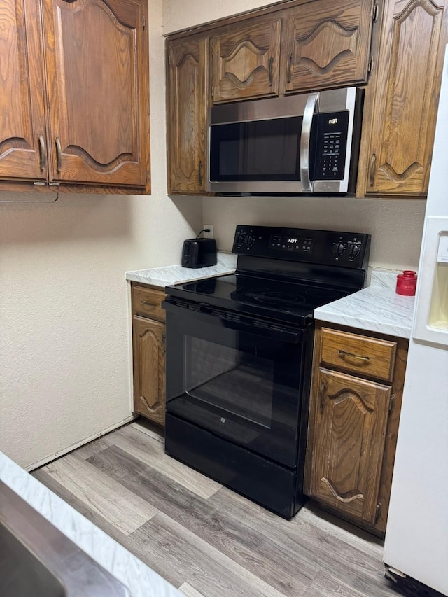 419 Travis St, Ranger, TX 76470 - kitchen featuring stainless steel microwave, black electric range, light countertops, white fridge with ice dispenser, and light wood-style floors