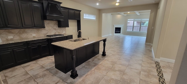 3805 Bentley Dr, Bedford, TX 76021 - kitchen featuring dark cabinetry, a sink, premium range hood, decorative backsplash, and stainless steel gas stovetop