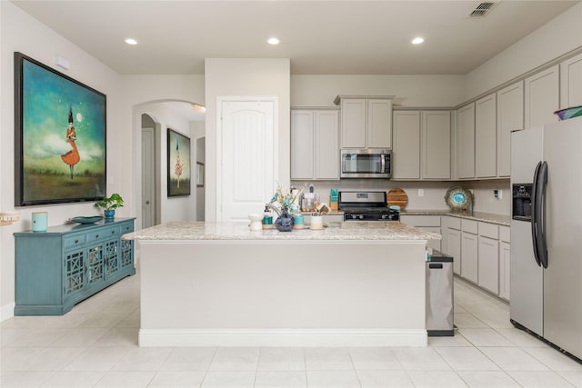 1909 Outpost Creek Ln, Aubrey, TX 76227 - kitchen featuring appliances with stainless steel finishes, arched walkways, a center island with sink, light stone countertops, and recessed lighting
