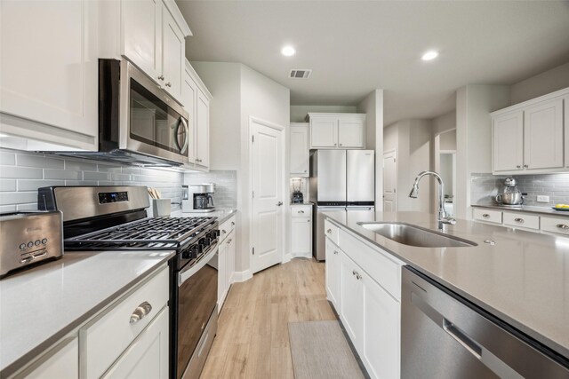 236 Mossy Cliff Ln, Fort Worth, TX 76052 - kitchen with stainless steel appliances, a sink, decorative backsplash, white cabinetry, and light wood-style flooring