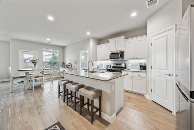 236 Mossy Cliff Ln, Fort Worth, TX 76052 - kitchen featuring appliances with stainless steel finishes, a sink, light wood-style flooring, an island with sink, and a breakfast bar