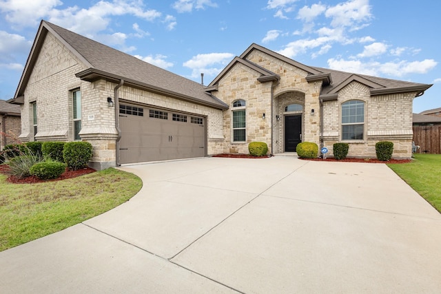 french country inspired facade featuring driveway, a shingled roof, an attached garage, and stone siding