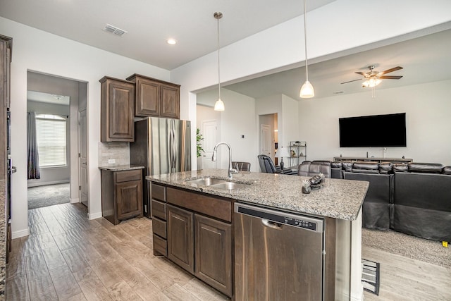 kitchen with stainless steel dishwasher, a sink, light wood-style floors, light stone counters, and recessed lighting