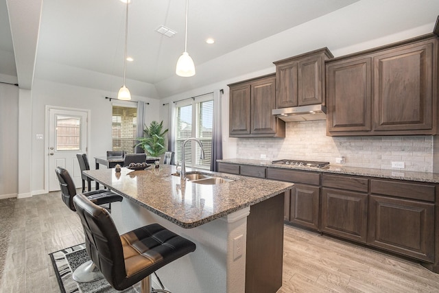 kitchen featuring a sink, light stone countertops, a breakfast bar area, backsplash, and vaulted ceiling
