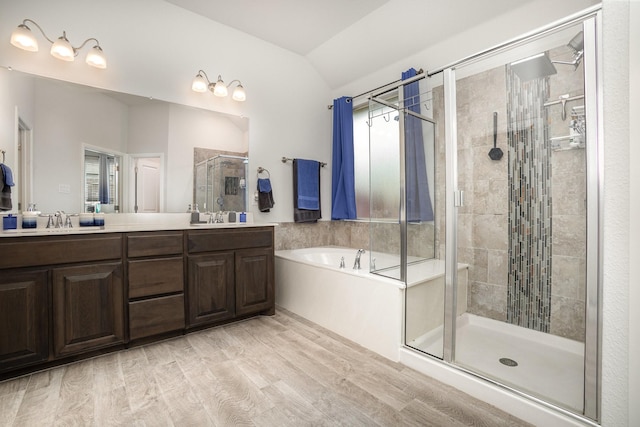 full bath featuring a stall shower, a bath, double vanity, lofted ceiling, and wood finished floors