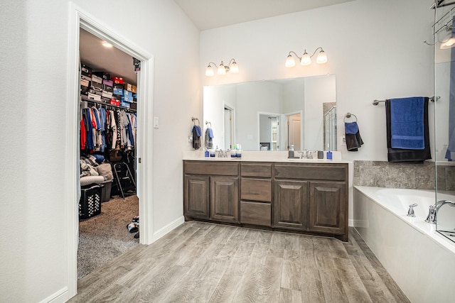 full bathroom with wood finished floors, double vanity, a bath, and a walk in closet