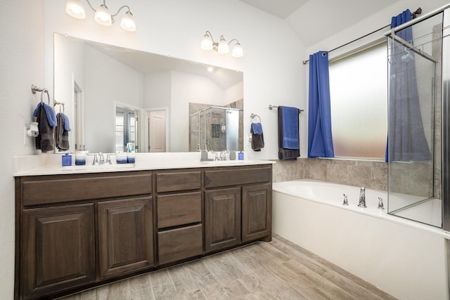 bathroom with a stall shower, wood finished floors, a bath, double vanity, and lofted ceiling