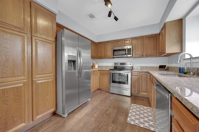 2434 Antler Trl, Lewisville, TX 75067 - kitchen with stainless steel appliances, a sink, light wood-type flooring, light stone countertops, and brown cabinets