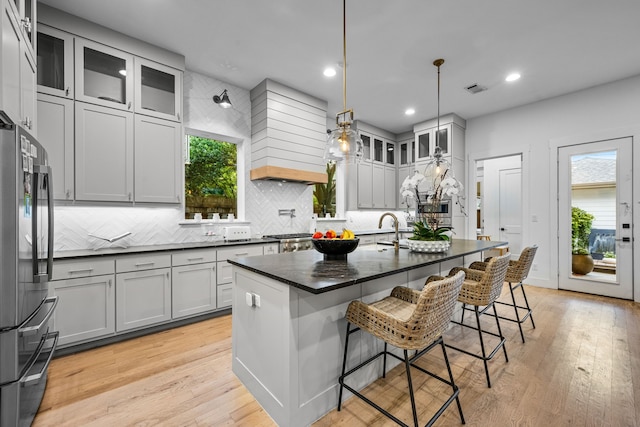 kitchen with freestanding refrigerator, custom exhaust hood, tasteful backsplash, a breakfast bar, and light wood-style floors