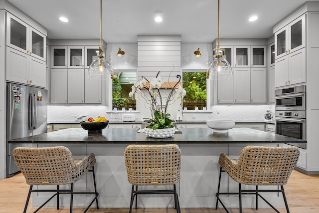 kitchen with appliances with stainless steel finishes, light wood-type flooring, tasteful backsplash, dark stone countertops, and recessed lighting