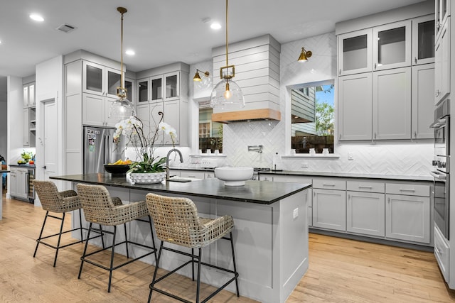 kitchen featuring stainless steel appliances, a sink, decorative backsplash, light wood-style flooring, and a kitchen island with sink