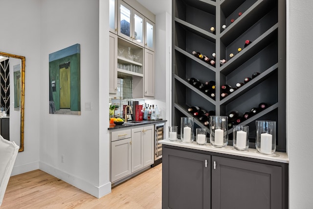 wine cellar featuring wet bar, light wood-style floors, beverage cooler, and baseboards