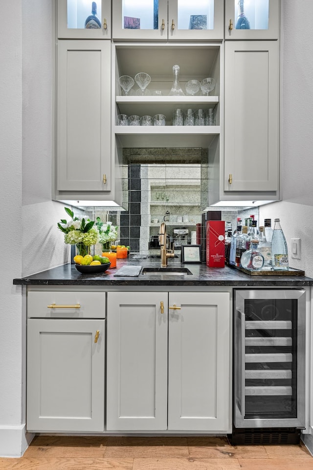 indoor wet bar featuring beverage cooler, light wood-style flooring, and decorative backsplash