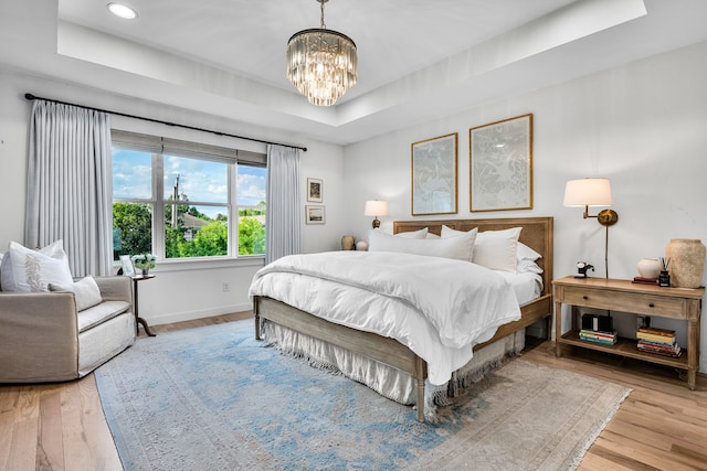bedroom with a raised ceiling, a chandelier, baseboards, wood finished floors, and recessed lighting
