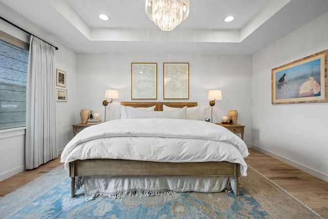 bedroom featuring wood finished floors, baseboards, a tray ceiling, a chandelier, and recessed lighting