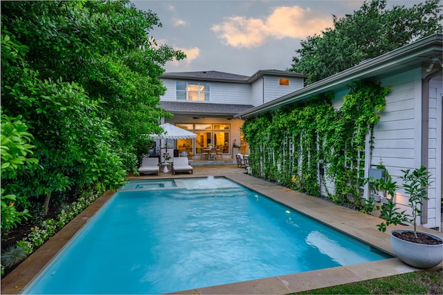pool at dusk featuring a patio and a pool with connected hot tub