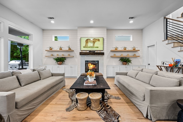 living room featuring stairway, light wood-type flooring, a large fireplace, and recessed lighting