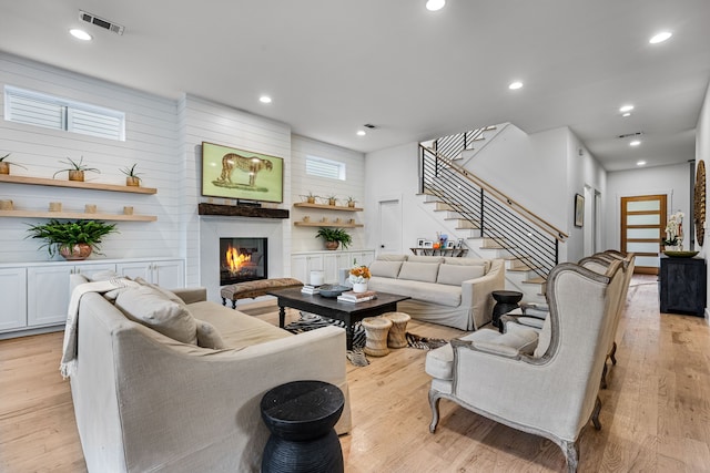 living area featuring stairs, a glass covered fireplace, light wood-style flooring, healthy amount of natural light, and recessed lighting