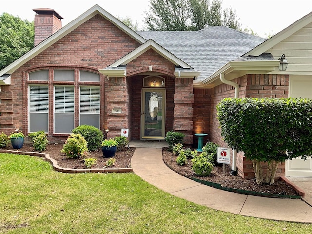 1913 Monte Cristo Way, Sherman, TX 75092 - view of exterior entry featuring a shingled roof, a chimney, brick siding, and a yard