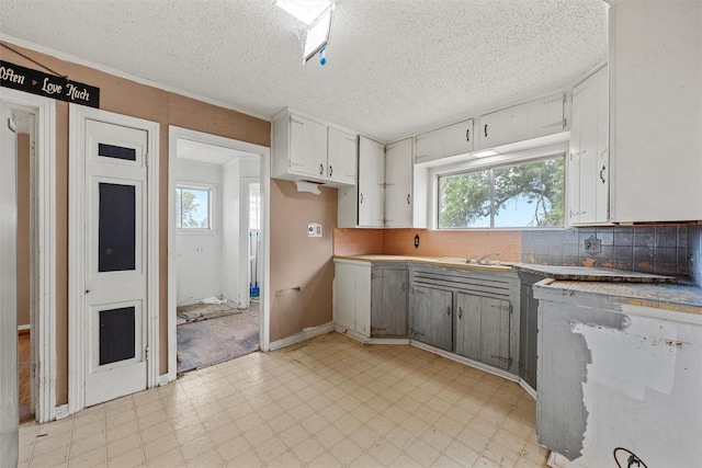 1677 Hobbs Ln, Waco, TX 76706 - kitchen featuring dishwasher, light flooring, a textured ceiling, tasteful backsplash, and white cabinets