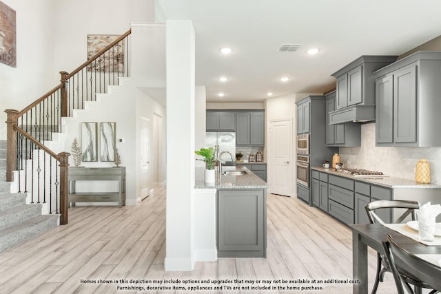 406 Maltese Cir, Wylie, TX 75098 - kitchen featuring appliances with stainless steel finishes, gray cabinetry, light wood-style floors, light stone counters, and decorative backsplash