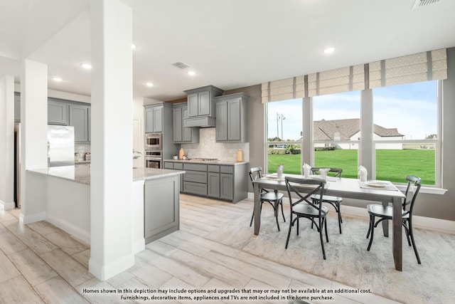 406 Maltese Cir, Wylie, TX 75098 - kitchen featuring gray cabinets, appliances with stainless steel finishes, tasteful backsplash, light stone countertops, and under cabinet range hood