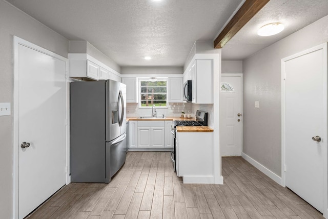 6012 Whispering Ln, Watauga, TX 76148 - kitchen with appliances with stainless steel finishes, a sink, white cabinets, a textured ceiling, and light wood-style flooring