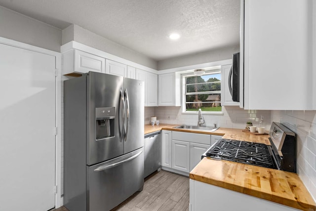 6012 Whispering Ln, Watauga, TX 76148 - kitchen with stainless steel appliances, a sink, wood counters, white cabinetry, and light wood-type flooring