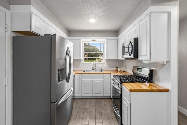 6012 Whispering Ln, Watauga, TX 76148 - kitchen featuring butcher block counters, stainless steel appliances, a sink, light wood finished floors, and a textured ceiling