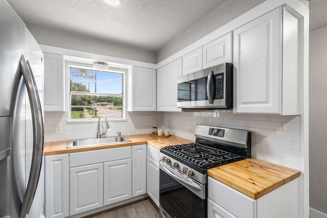 6012 Whispering Ln, Watauga, TX 76148 - kitchen with stainless steel appliances, a sink, butcher block counters, a textured ceiling, and decorative backsplash