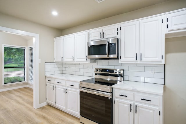 1202 Bayshore Dr, Rockwall, TX 75087 - kitchen with stainless steel appliances, backsplash, light wood finished floors, white cabinets, and baseboards