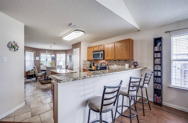 1312 Dakota Trl, Krum, TX 76249 - kitchen featuring stainless steel appliances, a peninsula, baseboards, backsplash, and a textured ceiling
