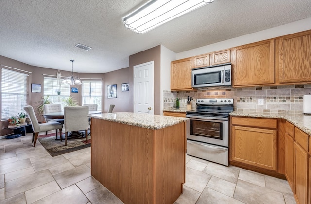 1312 Dakota Trl, Krum, TX 76249 - kitchen featuring appliances with stainless steel finishes, a center island, a textured ceiling, decorative backsplash, and a chandelier
