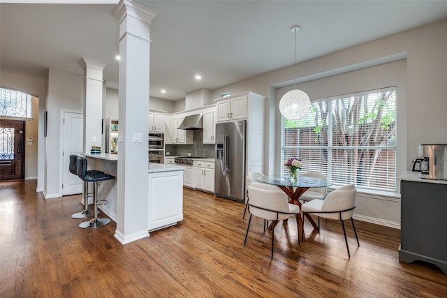 5001 Stanford Ave, Dallas, TX 75209 - kitchen featuring appliances with stainless steel finishes, wall chimney range hood, light countertops, wood finished floors, and white cabinetry