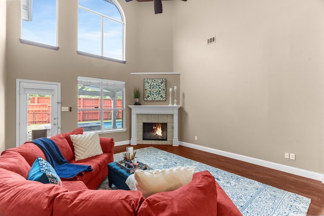 9772 Hickory St, Frisco, TX 75035 - living area featuring a ceiling fan, wood finished floors, baseboards, a fireplace, and a towering ceiling