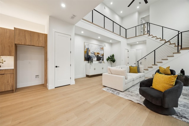 5217 Lindsley Ave, Dallas, TX 75223 - living area featuring light wood-type flooring, stairs, a ceiling fan, a towering ceiling, and baseboards