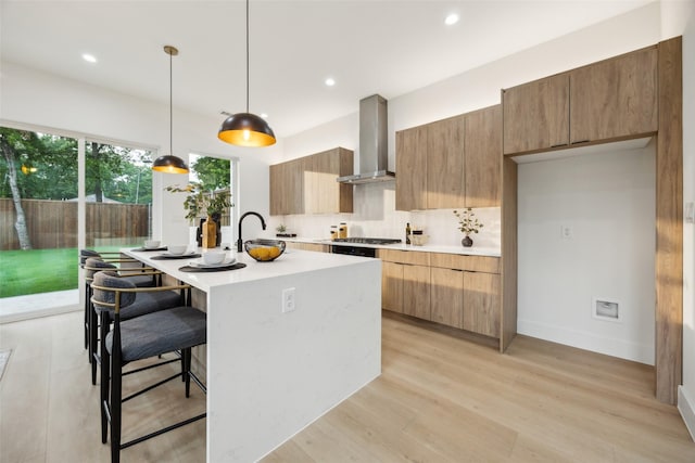 5217 Lindsley Ave, Dallas, TX 75223 - kitchen with wall chimney exhaust hood, light countertops, modern cabinets, a kitchen island with sink, and a kitchen bar