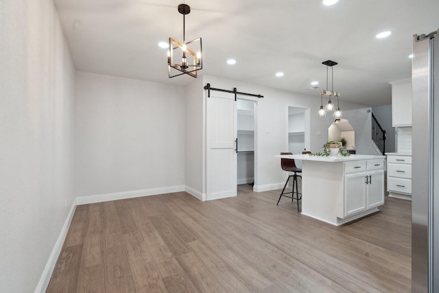 2123 Wheaton Dr, Richardson, TX 75081 - kitchen with a barn door, baseboards, white cabinets, light wood-type flooring, and a kitchen breakfast bar
