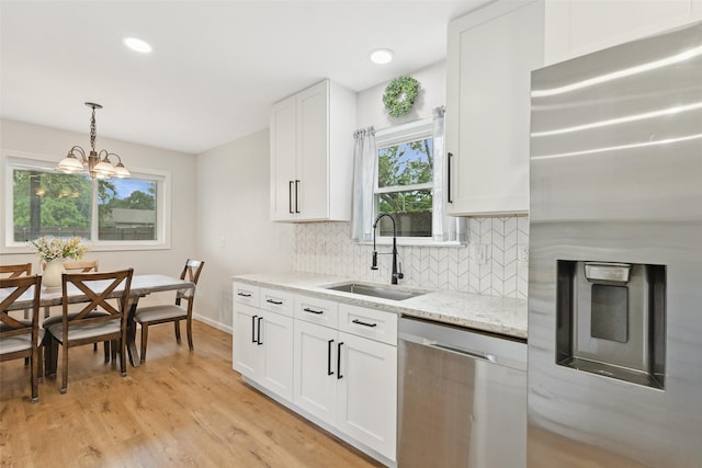 kitchen featuring appliances with stainless steel finishes, a sink, backsplash, light wood-style floors, and white cabinetry