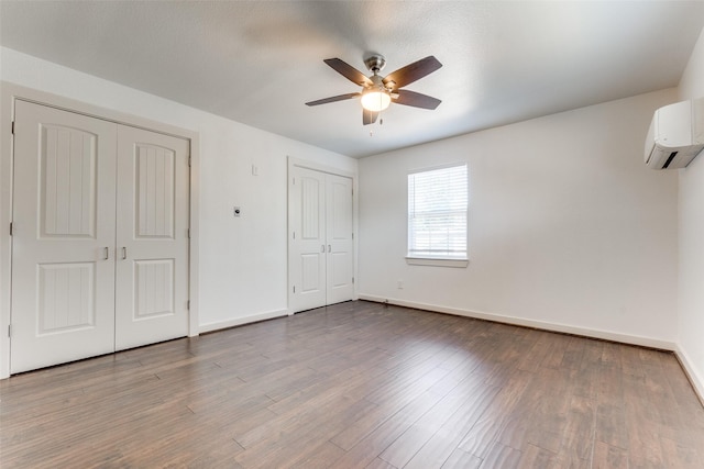 8919 San Fernando Way, Dallas, TX 75218 - unfurnished bedroom featuring multiple closets, an AC wall unit, baseboards, and wood finished floors