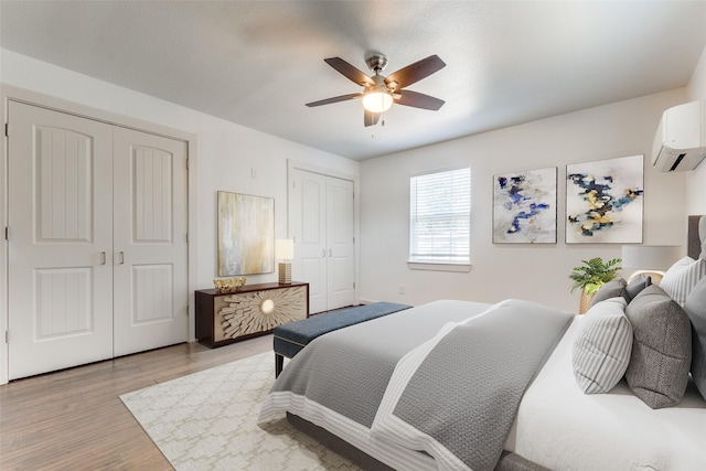 8919 San Fernando Way, Dallas, TX 75218 - bedroom featuring a wall mounted AC, multiple closets, light wood-style floors, and a ceiling fan