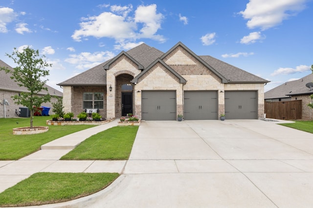 509 Oleander Dr, Royse City, TX 75189 - french country style house with concrete driveway, an attached garage, roof with shingles, central air condition unit, and stone siding