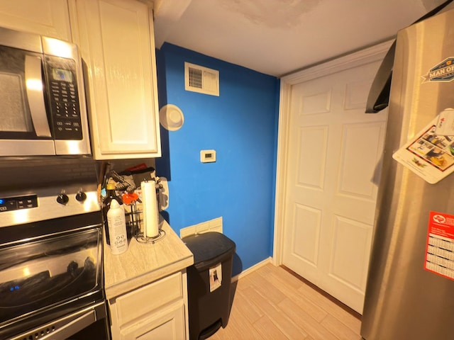 kitchen with stainless steel appliances, light wood-type flooring, baseboards, and white cabinetry