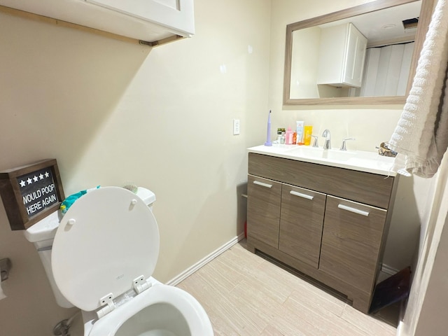 half bathroom featuring baseboards, toilet, and vanity