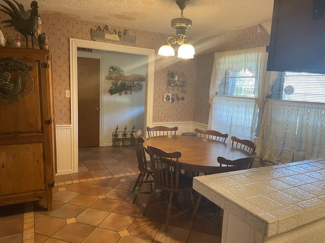 909 Mckinney Ave, Princeton, TX 75407 - dining space with wallpapered walls, wainscoting, a textured ceiling, and light tile patterned floors