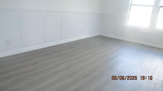 unfurnished room with wood finished floors, baseboards, and a decorative wall