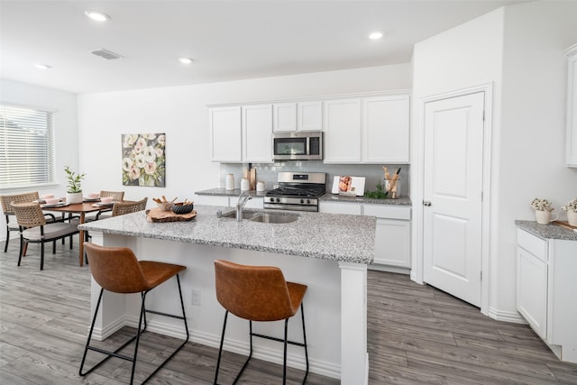 5836 Priory Dr, Celina, TX 76227 - kitchen with appliances with stainless steel finishes, a sink, wood finished floors, a kitchen bar, and white cabinets