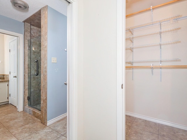 905 High Rd, Coleman, TX 76834 - full bath featuring a stall shower, a walk in closet, baseboards, and tile patterned floors