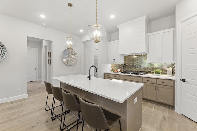 1015 Olympic Dr, Rockwall, TX 75087 - kitchen featuring custom exhaust hood, backsplash, light wood-type flooring, a kitchen breakfast bar, and light countertops