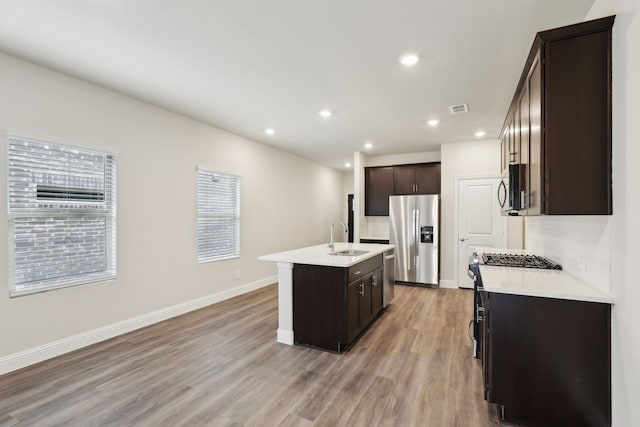 519 Willet Dr, Mckinney, TX 75069 - kitchen with appliances with stainless steel finishes, a sink, dark brown cabinets, light wood-type flooring, and an island with sink